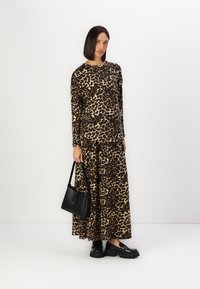 Majica z dolgimi rokavi z leopardjim vzorcem in ujemajoča krila iz mehkega materiala. Črna torbica in debeli črni čevlji dopolnjujejo obleko.