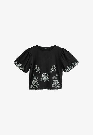 Schwarze Bluse mit kurzen Puffärmeln und weißer Blumenstickerei auf der Vorderseite, den Ärmeln und dem gewellten Saum.