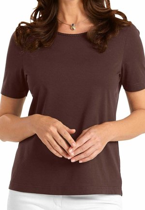 Brun t-shirt med korte ærmer, rund halsudskæring og glat tekstur. Har en dekorativ syning langs kraven. Båret med hvide bukser.