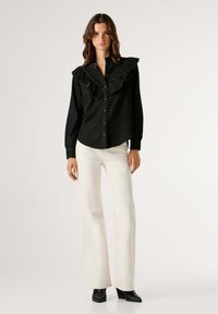 Čierna džínsová košeľa s volánovým golierom, zapínaním na gombíky vpredu a dlhými rukávmi. Kombinovaná s bielymi zvonovými nohavicami a čiernymi čižmami na opätku.