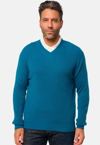 Pull à col en V en teal avec texture côtelée, manches longues et coupe décontractée, associé à une chemise blanche à col en dessous.