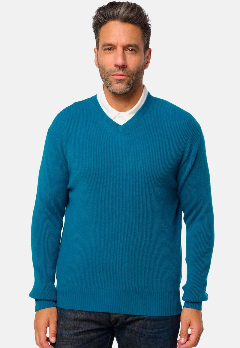 Pull à col en V en teal avec texture côtelée, manches longues et coupe décontractée, associé à une chemise blanche à col en dessous.