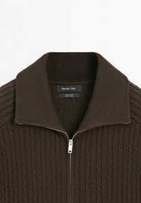 Donkerbruine kabelgebreide katoenen trui met een hoge kraag en een zilveren rits aan de voorkant, gelabeld "Massimo Dutti," gemaakt in China.