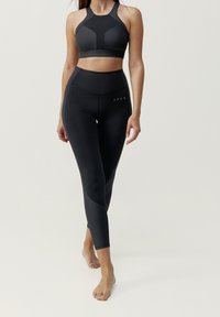 Czarny sportowy stanik i dopasowane legginsy o wysokim stanie, wykonane z gładkiego, elastycznego materiału z geometrycznymi detalami i przylegającym krojem.