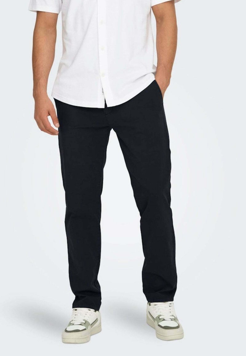 Pantaloni neri realizzati in tessuto leggero, design a gamba dritta, abbinati a sneakers bianche. Texture liscia senza motivi o accenti visibili.