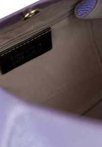 Interno di una borsa in pelle viola che mostra una fodera beige, una tasca con zip e un'etichetta del marchio con testo impresso che indica la lavorazione italiana.