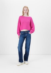 Pull en maille, rose, court avec un design texturé ; associé à un jean bleu droit avec une fermeture à boutons et un léger délavage.