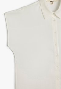 Blusa bianca a maniche corte con colletto classico, chiusura anteriore con bottoni e tessuto morbido. Presenta una vestibilità rilassata e senza motivi visibili.
