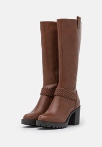 Bruine leren laarzen tot de knie met een geweven banddetail bij de enkel, stevige hak en een gestructureerde zool voor grip. Rits aan de zijkant.