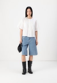Hvit kortermet bluse med pintuck-detaljer, kombinert med lyseblå denim-bukser. Sorte knelang støvler og en svart håndveske fullfører antrekket.