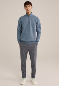 Ljusblå fleece zip-up tröja med långa ärmar, kombinerad med grå skräddarsydda byxor och vita sneakers. Slät textur, avslappnad design.