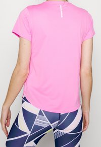 Pink, short-sleeve athletic shirt with a subtle texture, featuring a rounded neckline and logo on the upper back. Paired with patterned leggings.