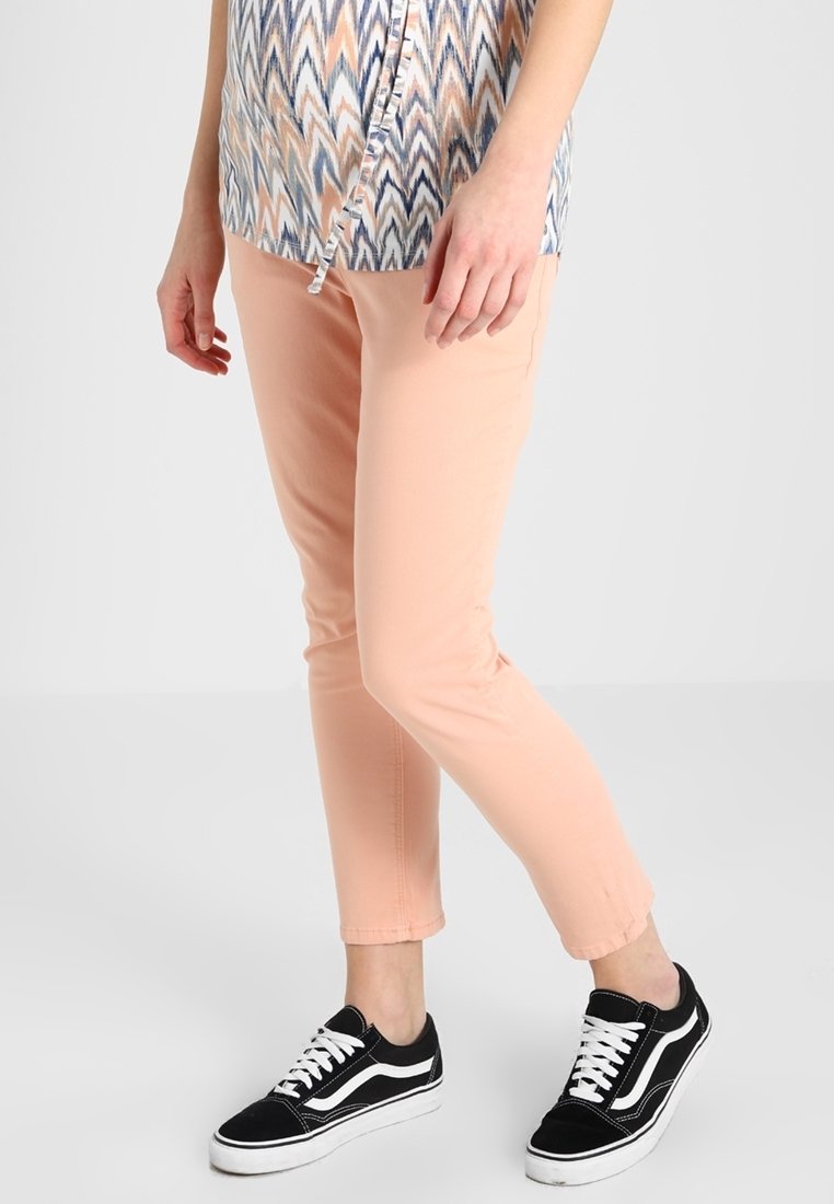 Pantalon en coton rose à coupe slim, associé à des baskets en toile noire avec des accents blancs. Le haut présente un motif en zigzag bleu et pêche.