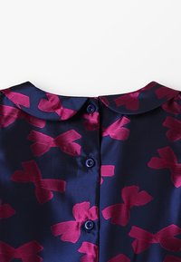 Abito blu navy in tessuto lucido, con un motivo di fiocchi fucsia. Presenta un colletto rotondo e due bottoni sul retro.