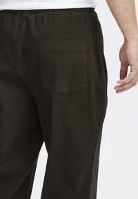 Svarte joggebukser laget av myk stoff, med en enkelt baklomme og elastisk midje for komfort.