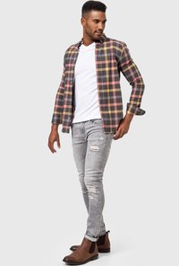 Camisa de franela a cuadros en gris oscuro, rosa y amarillo; camiseta blanca debajo; jeans desgastados en gris claro; botas Chelsea marrones.