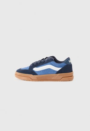 Sneakers en daim bleu avec une bande latérale blanche, une semelle en caoutchouc brun et des accents bleu foncé contrastants. Les lacets plats complètent le design.