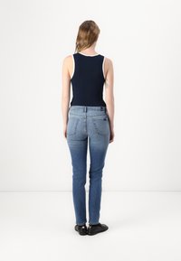 Navy tank top with white trim, paired with fitted blue denim jeans. Cotton blend materials, no visible patterns, and flat black shoes.