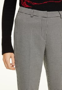Pantalon en tissu à motif pied-de-poule noir et blanc avec une coupe cintrée, doté de passants de ceinture et de poches latérales, fabriqué dans un tissu texturé.