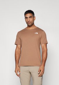 Camiseta de manga corta marrón hecha de una tela suave con cuello redondo, que presenta un logo blanco en la parte superior izquierda del pecho.