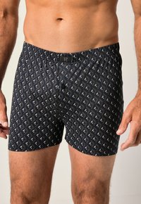 Boxer da uomo neri con un design geometrico bianco e beige. Presentano un elastico in vita e una patta con bottone anteriore.