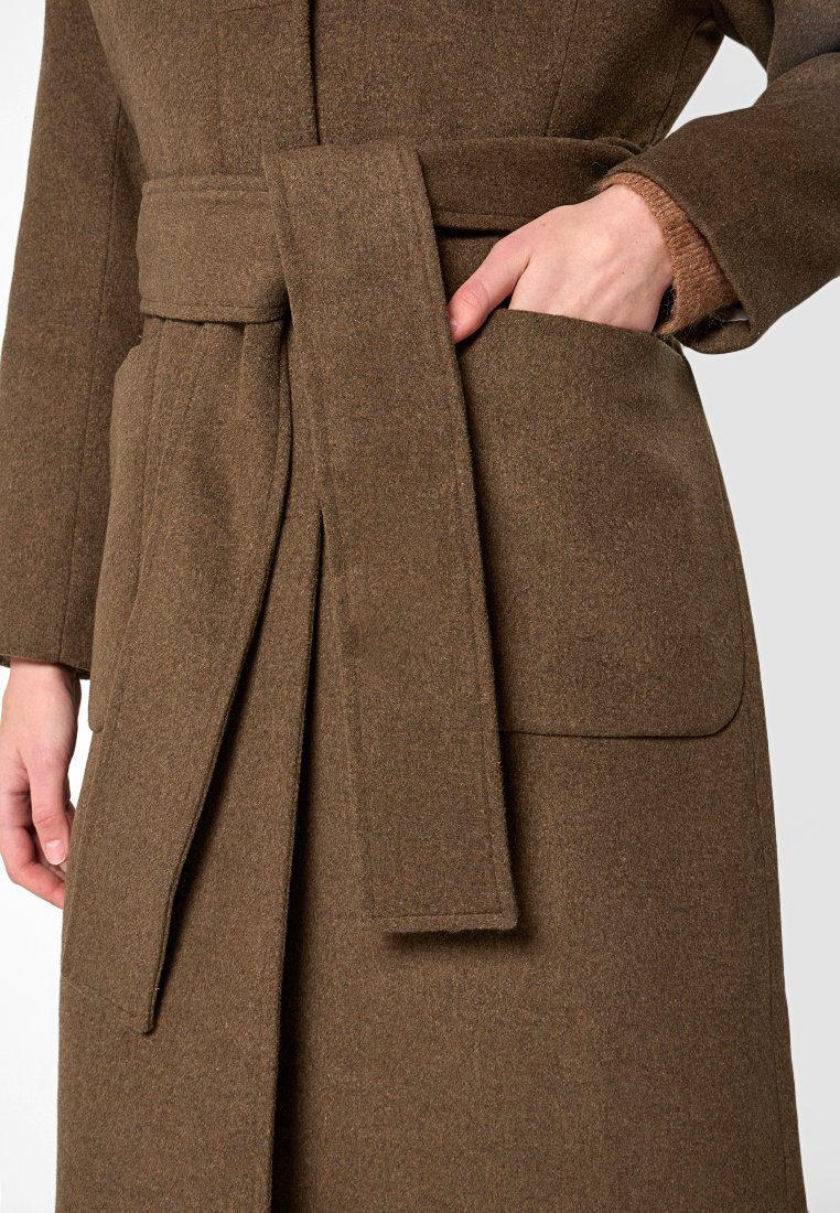 Brauner Wollmantel mit breitem Gürtel, seitlichen Taschen und klassischem Kragen. Die Textur wirkt weich und leicht fusselig.