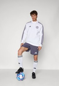 Hvit adidas-hettegenser med logo og tre striper, kombinert med grå shorts med striper, hvite sokker, svarte fotballsko og en fotball.