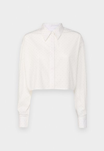 Camicia bianca tagliata con maniche lunghe, colletto abbottonato e motivo a piccoli pois. Realizzata in tessuto morbido, presenta una vestibilità rilassata.