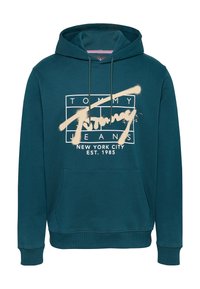 Sudadera de algodón color teal con un bolsillo frontal, capucha con cordones y texto gráfico blanco "TOMMY JEANS NEW YORK CITY EST. 1985" en un diseño rectangular.