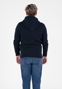 Felpa con cappuccio di colore blu navy, realizzata in tessuto morbido, caratterizzata da maniche lunghe, orlo arrotondato e una vestibilità casual, abbinata a jeans in denim blu.