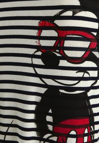 Souris de dessin animé portant de grandes lunettes rouges et un short rouge, imprimée sur un tissu à rayures horizontales blanches et noires.