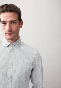 Camicia a righe con bottoni, caratterizzata da una combinazione di colori blu e bianco, colletto classico, taschino frontale e vestibilità regolare. Il tessuto testurizzato dona profondità.