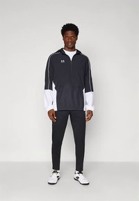 Mustvalge poole tõmblukuga tuulejaak, millel on peegeldavad aktsendid, eesmine tasku, kombineeritud mustade sobivate dressipükste ja valgete tossudega.