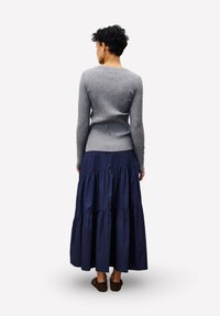 Grauer gerippter Pullover, kombiniert mit einem marineblauen, gestuften Maxirock. Das Outfit hat ein eng anliegendes Oberteil und einen fließenden, strukturierten Rock. Braune Schuhe vervollständigen den Look.