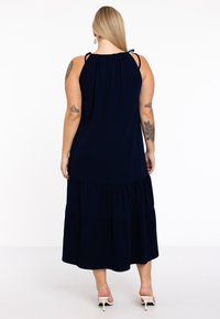 Navyblaues Maxikleid mit Spaghetti-Trägern, gerafftem Ausschnitt und geschichteten Rüschendesign am Saum, gefertigt aus einem weichen, flexiblen Stoff.