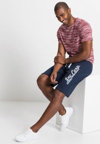 T-shirt a righe rosse e bianche con maniche corte, abbinato a pantaloni corti blu con grafiche bianche. Scarpe da ginnastica bianche completano l'outfit.