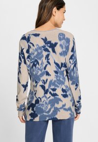 Beiger Pullover mit dunkelblauem Blumenmuster, langen Ärmeln und geripptem Saum. Weiche Textur mit lockerem Schnitt und weitem Ausschnitt.