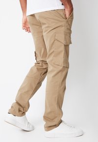 Beige cargobukser med et design med lige ben, flere sidelommer og et let bomuldsmateriale, kombineret med hvide sneakers.