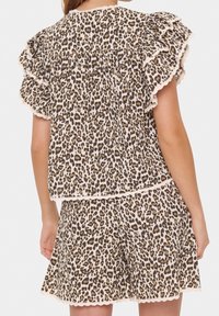 Zestaw bluzki i szortów w cętki z falbankami, falbaniastymi krawędziami oraz miękkiego, lekkiego materiału w neutralnych odcieniach.