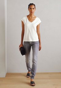 Witte T-shirt met korte mouwen en V-hals, gecombineerd met vervaagde grijze skinny jeans. Draagt het met platte zwarte sandalen en een zwarte clutch in de hand.