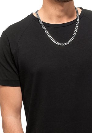 Homme portant une chaîne en argent sur un t-shirt noir uni à manches courtes et col rond, visible du cou jusqu'au milieu du torse.