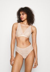 Spitzen-Bralette und hochgeschnittene Panty in Nude-Farbe mit floralen Mustern und gewellten Kanten. Weicher Stoff, keine Polsterung oder Bügel.
