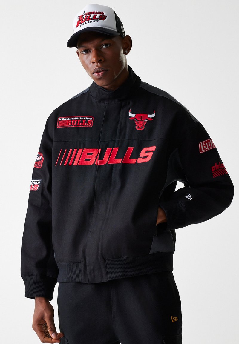 Black jacket with red "BULLS" lettering and embroidered logos, featuring a high collar and ribbed cuffs, paired with a white and black cap.