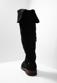 Czarne zamszowe kozaki za kolano z wywiniętym mankietem, płaskim obcasem, zamkiem błyskawicznym po boku oraz teksturowanym wzorem na cholewce.