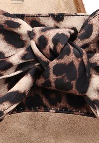 Tela de estampado de leopardo con un diseño anudado, sobre un fondo de ante beige. Apariencia texturada y suave con patrones oscuros contrastantes.