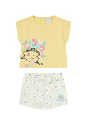 Camiseta amarilla de manga corta para bebé con una niña sonriente y flores, combinada con pantalones cortos blancos con estampados florales en turquesa y amarillo y un lazo.
