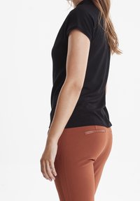 Černá polokošile s krátkým rukávem a přiléhavým střihem, doplněná o kalhoty v rezavé barvě s mírným koženým akcentem na zadní kapse.