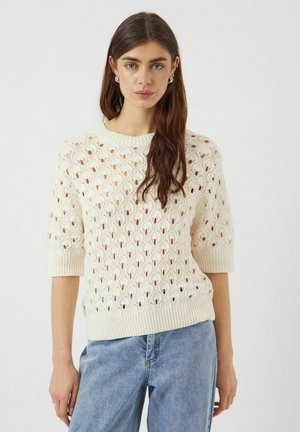 Cremefarvet strikket sweater med et struktureret, åbent blonderdesign, korte ærmer samt ribbet krave og kant. Kombineret med lyseblå jeans.