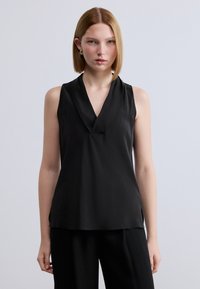 Μαύρο αμάνικο τοπ με βαθύ V-λαιμόκοψη και σχεδιασμό με πτυχώσεις. Ομαλό, ελαφρύ ύφασμα με άνετη εφαρμογή, συνδυασμένο με φαρδιά μαύρη παντελόνα.