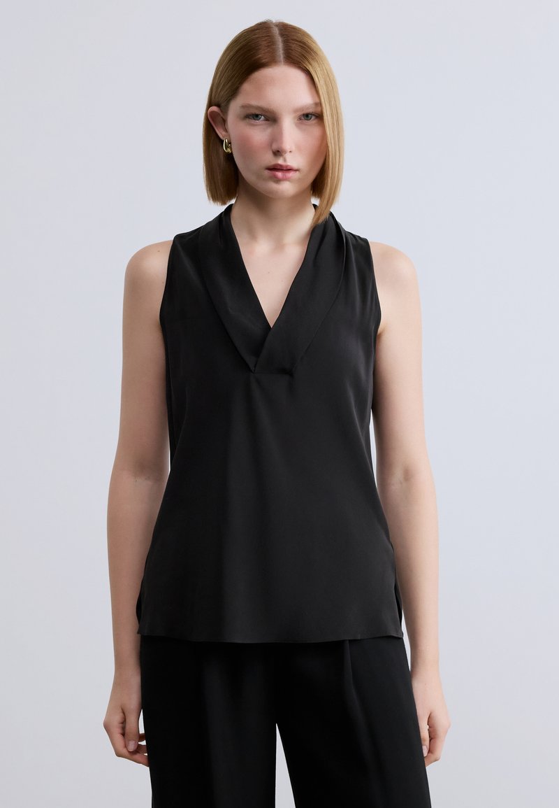 Μαύρο αμάνικο τοπ με βαθύ V-λαιμόκοψη και σχεδιασμό με πτυχώσεις. Ομαλό, ελαφρύ ύφασμα με άνετη εφαρμογή, συνδυασμένο με φαρδιά μαύρη παντελόνα.